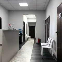 Korytarz przychodni z recepcją, drzwiami i białymi krzesłami.