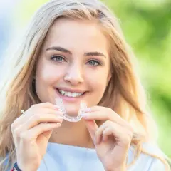 Uśmiechnięta blondynka prezentuje przezroczysty aparat Invisalign, dowód na jego dyskretne działanie i piękne efekty.