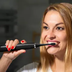 Kobieta z czerwonymi paznokciami używa czarnej szczoteczki sonicznej do zębów.