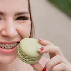 Uśmiechnięta dziewczyna z aparatem ortodontycznym trzyma zielonego makaronika. Pytanie: co jeść po założeniu aparatu?