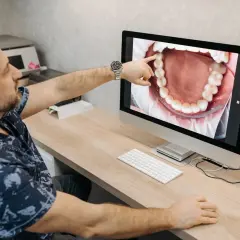 Dentysta pokazuje pacjentowi na monitorze zdjęcie jamy ustnej, wskazując na zdrową kieszonkę dziąsłową.