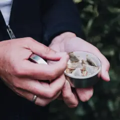 Dłoń wyjmuje z metalowego pudełka porcję snusu, który umieszcza się pod wargą, a nie na zęby.