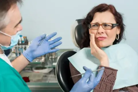 Kobieta z bólem zęba u dentysty. Lekarz w rękawiczkach pokazuje narzędzia, sugerując leczenie.