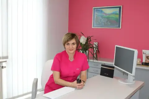 Lekarka w gabinecie dermatologii estetycznej, siedzi przy biurku z komputerem.