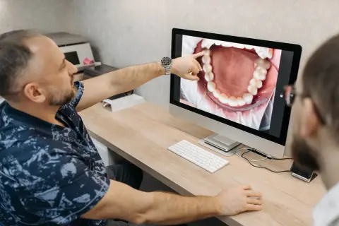 Dentysta pokazuje pacjentowi na monitorze zdjęcie jamy ustnej, wskazując na zdrową kieszonkę dziąsłową.