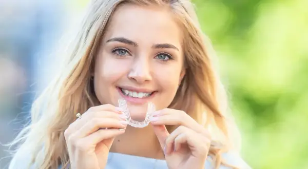 Uśmiechnięta blondynka prezentuje przezroczysty aparat Invisalign, dowód na jego dyskretne działanie i piękne efekty.