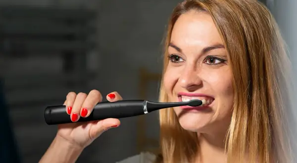 Kobieta z czerwonymi paznokciami używa czarnej szczoteczki sonicznej do zębów.