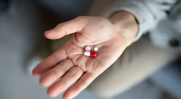 Dłoń trzyma garść tabletek, w tym kapsułkę i dwie mniejsze pigułki. To antybiotyk po wyrwaniu zęba, który pomoże w leczeniu.