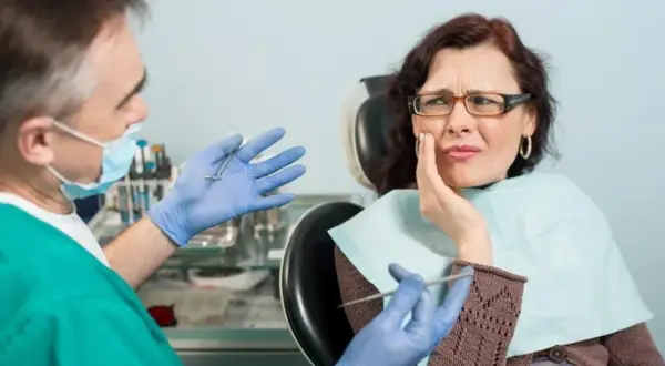 Kobieta z bólem zęba u dentysty. Lekarz w rękawiczkach pokazuje narzędzia, sugerując leczenie.