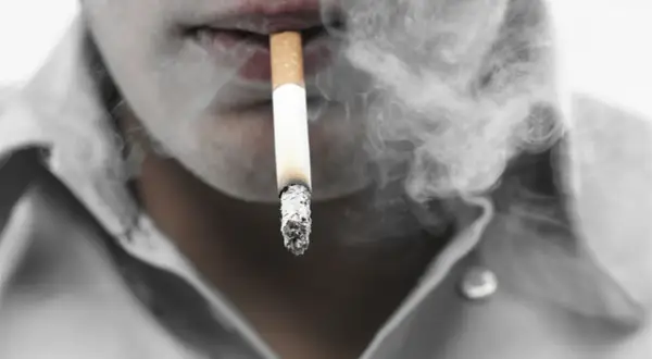 Dym papierosowy otacza usta, sugerując zatrucie nikotyną.