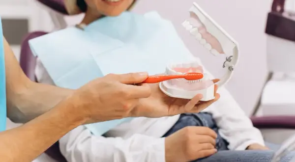 Dentysta pokazuje na modelu, jak prawidłowo szczotkować zęby, by zapobiegać ubytkom klinowym.