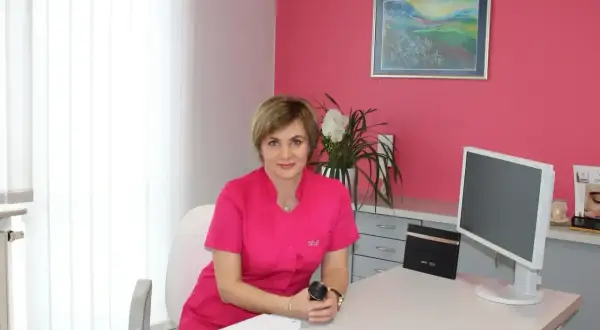 Lekarka w gabinecie dermatologii estetycznej, siedzi przy biurku z komputerem.