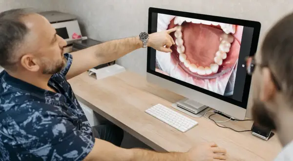 Dentysta pokazuje pacjentowi na monitorze zdjęcie jamy ustnej, wskazując na zdrową kieszonkę dziąsłową.