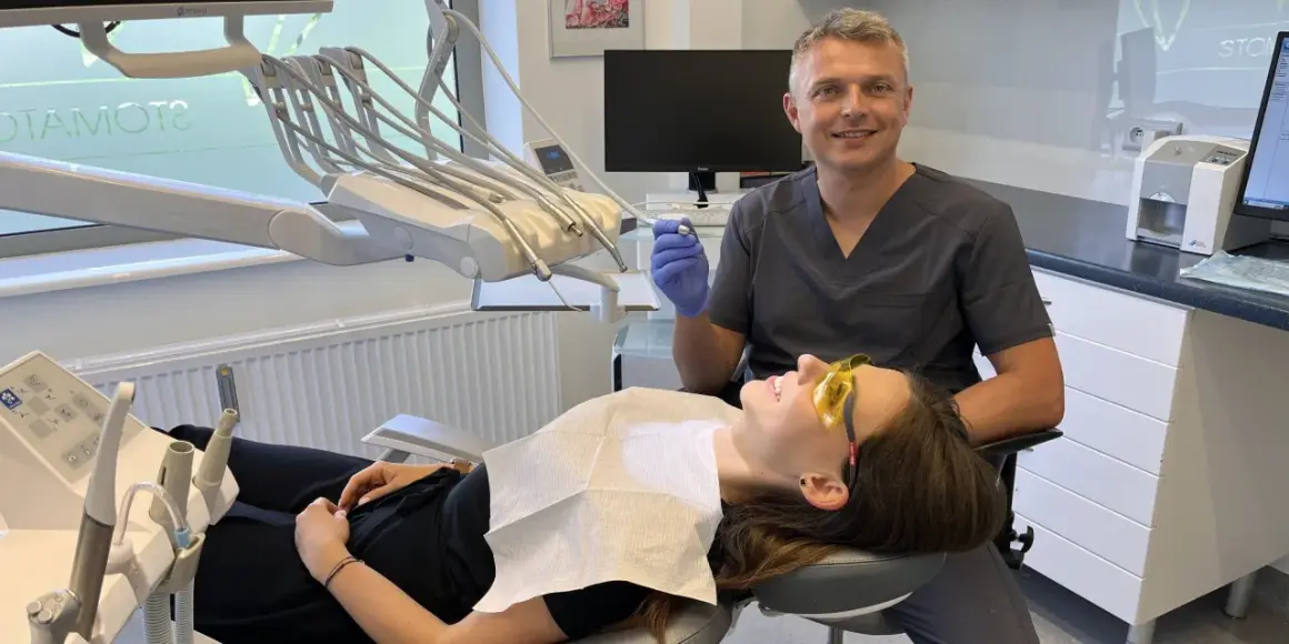 Dentysta w rękawiczce trzyma wiertło, pacjentka w okularach ochronnych leży na fotelu.