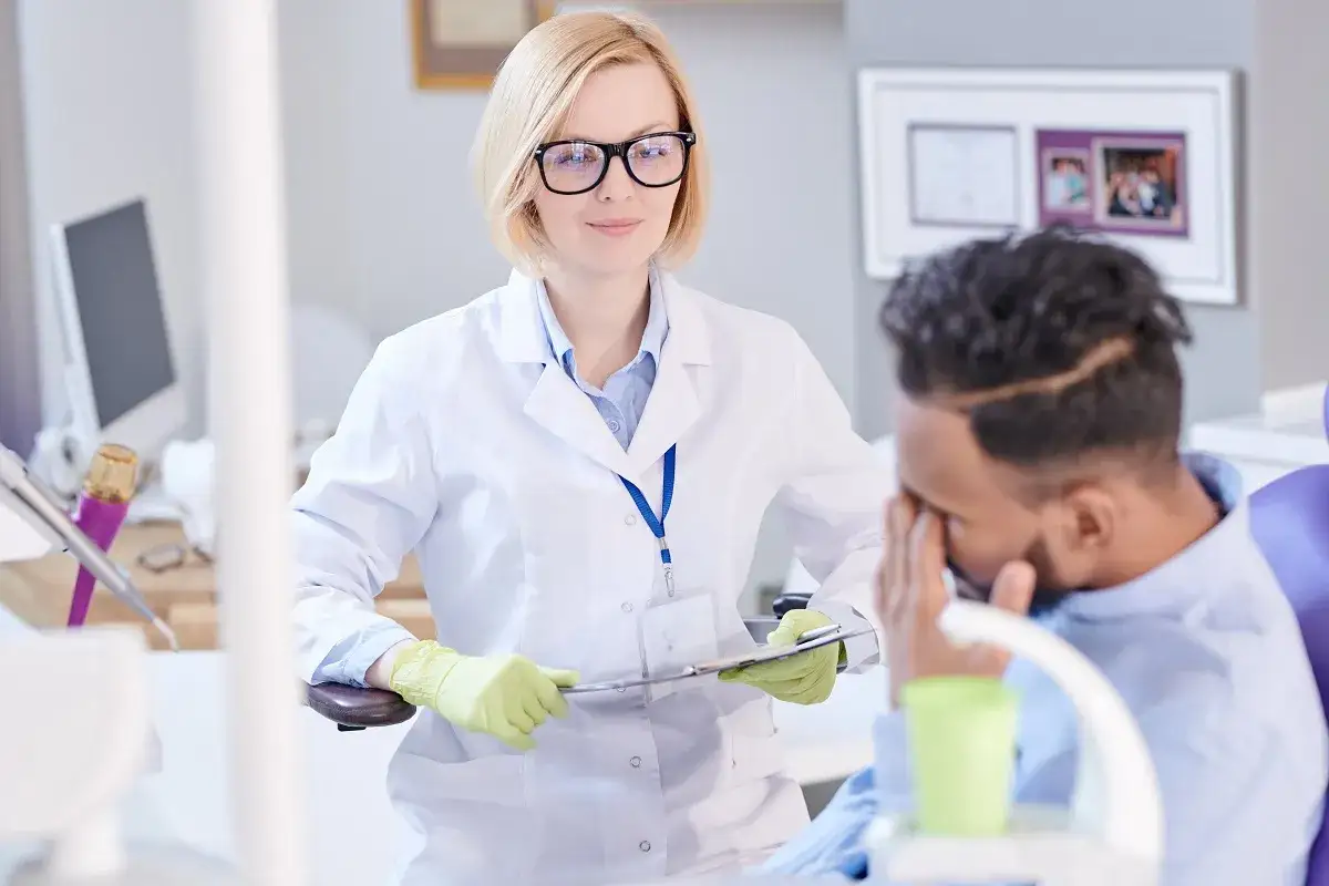 Dentystka w białym fartuchu i rękawiczkach rozmawia z pacjentem. Czy dentysta może wystawić L4?