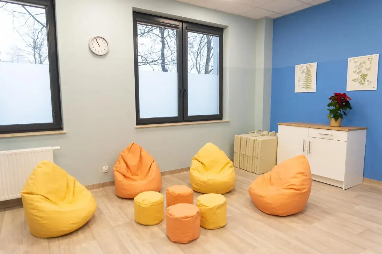 Kolorowe pufy i stoliki w jasnym pokoju terapeutycznym z oknami.