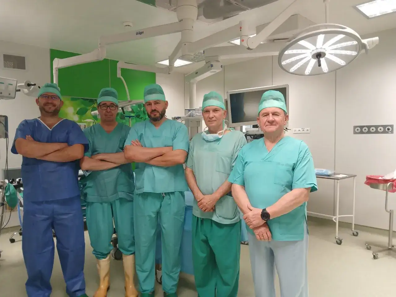 Pięciu chirurgów w zielonych i niebieskich strojach operacyjnych stoi w sali operacyjnej.