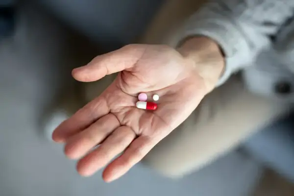 Dłoń trzyma garść tabletek, w tym kapsułkę i dwie mniejsze pigułki. To antybiotyk po wyrwaniu zęba, który pomoże w leczeniu.