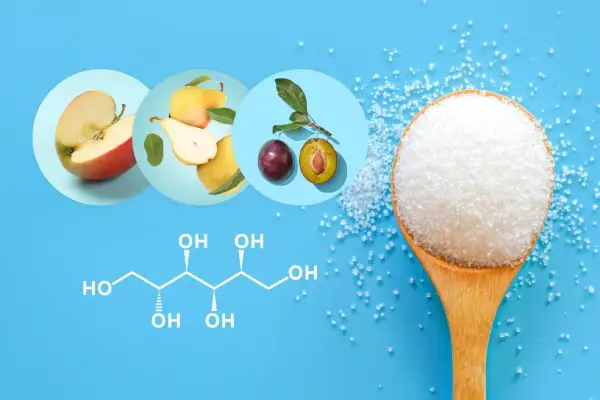 Jabłka, gruszki, śliwki i kryształki cukru na łyżce. Chemiczny wzór sorbitolu wyjaśnia, sorbitol co to jest.