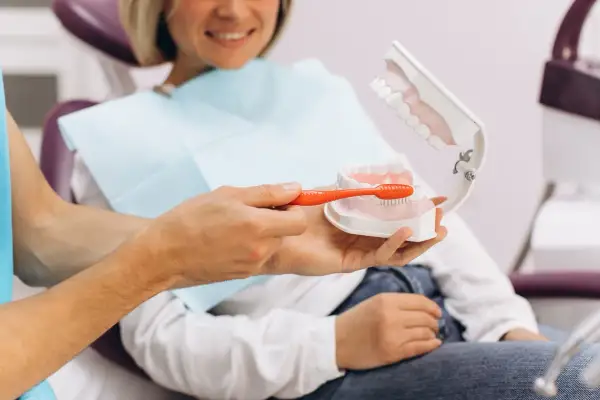 Dentysta pokazuje na modelu, jak prawidłowo szczotkować zęby, by zapobiegać ubytkom klinowym.