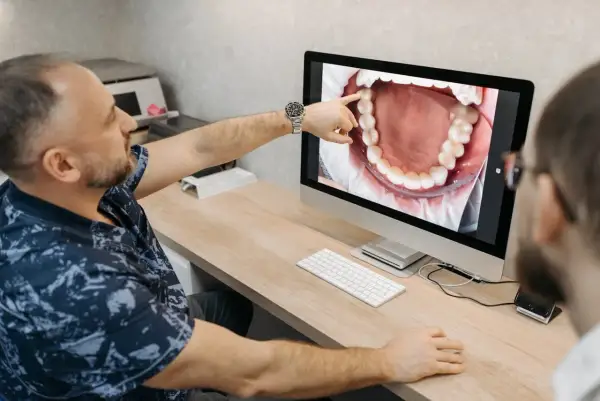 Dentysta pokazuje pacjentowi na monitorze zdjęcie jamy ustnej, wskazując na zdrową kieszonkę dziąsłową.