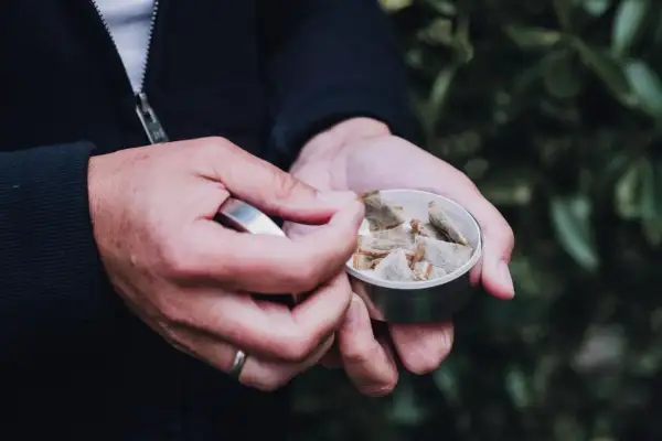 Dłoń wyjmuje z metalowego pudełka porcję snusu, który umieszcza się pod wargą, a nie na zęby.